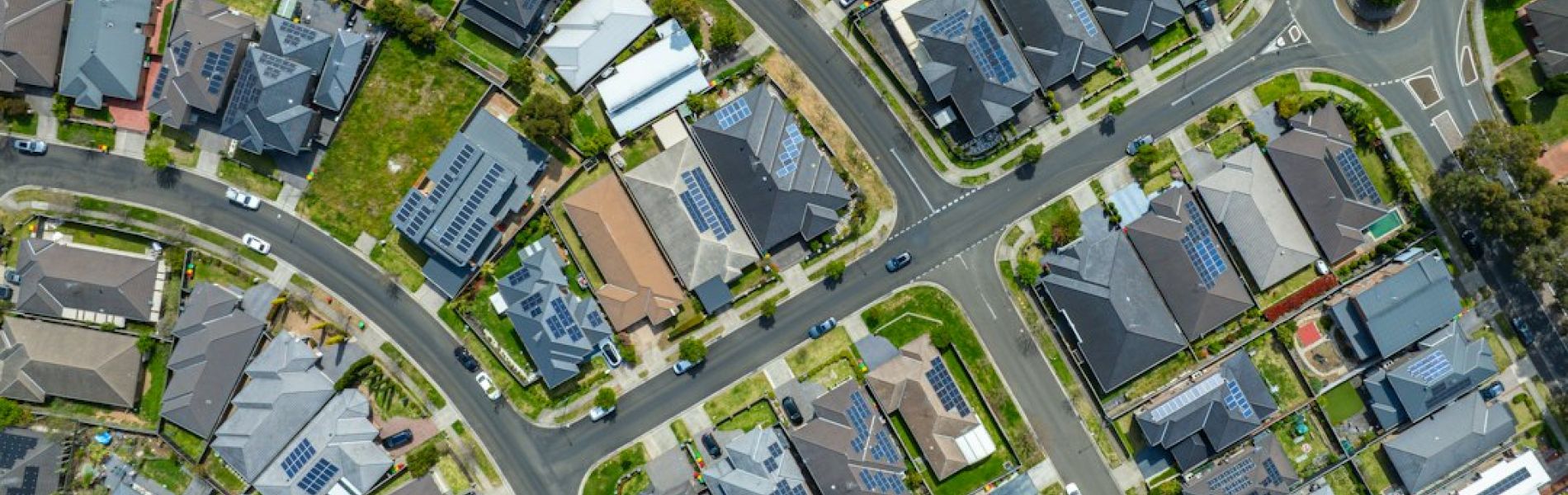 Vista aérea de urbanización residencial con casas unifamiliares equipadas con paneles solares en azoteas y jardines verdes