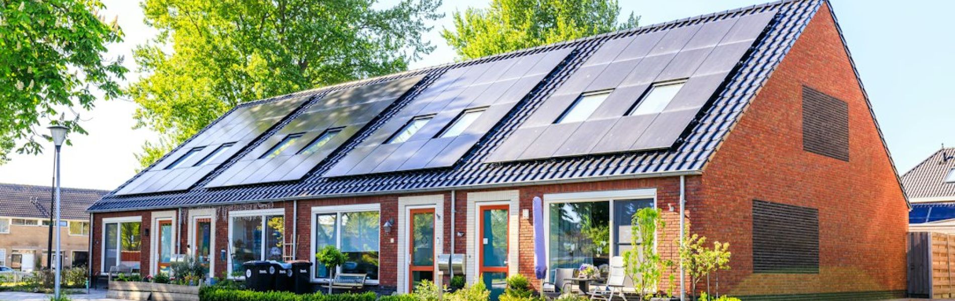 Casa moderna de ladrillo rojo con paneles solares instalados en tejado inclinado y jardín frontal